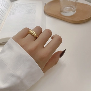 Detail shot of a polished golden twisted rope knot ring worn on index finger in a lifestyle setting