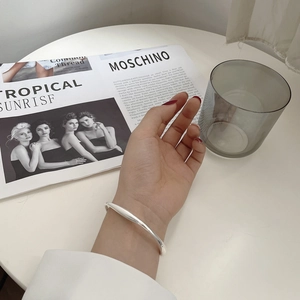 Irregular fluid design S925 sterling silver bangle shown on model's wrist with lifestyle decor