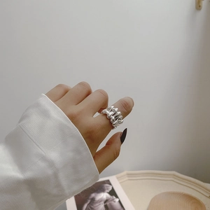 Detail view of silver braided chain ring on finger showing modern textured metal finish