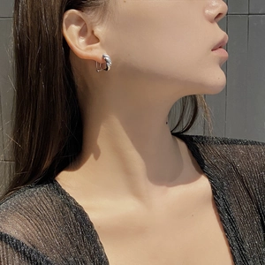 Detailed close-up of a twisted silver wave earring worn by a model in soft side lighting