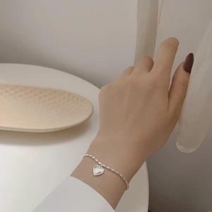 Detailed close-up of a silver heart charm bracelet with oval bead chain on wrist