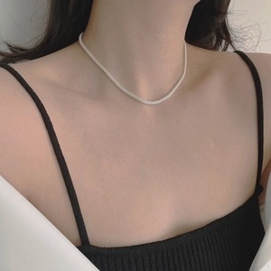 Detail shot of a flexible silver mesh chain necklace on model with woven metallic texture