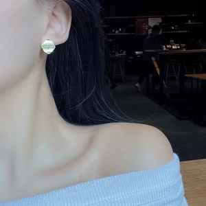 Detailed view of irregular geometric gold earrings worn by a model in a cafe setting