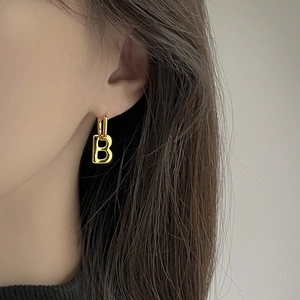 Detailed close-up of a gold-plated letter B drop earring worn on a model's ear