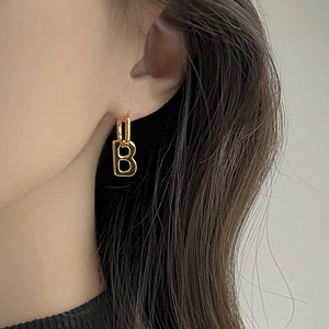 Macro side view of a gold-plated letter B drop earring on a model ear lobe
