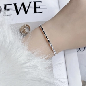 Minimalist silver wavy bangle with unique rippled texture shown on a wrist with magazine