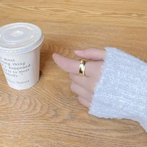 Close-up of a wide square gold ring with mirror finish worn on a finger over a wooden desk