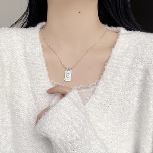 Macro detail of silver G-letter square pendant with hammered texture on ball chain