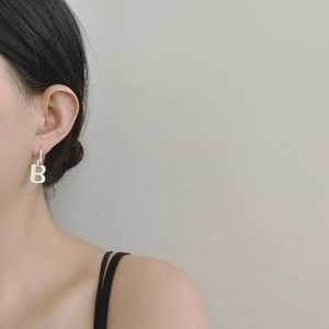 Close-up of minimalist silver letter B pendant earring worn on a female model