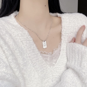 Detail of G letter wrinkled rectangular pendant necklace worn on a white sweater