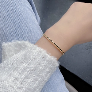 Close-up of a gold wavy sterling silver bangle with zircon stones worn on the wrist
