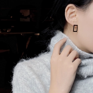 Close-up of golden rectangular hollow stud earrings worn by a model in a cozy setting