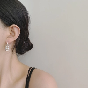 Close-up of minimalist silver letter B earrings worn by model for a modern fashion look