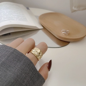 Detail view of a gold-plated irregular textured wide band ring worn on a finger