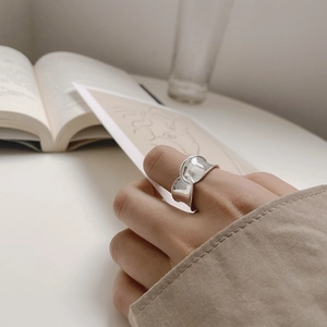 Close-up of a wide silver S925 cross-over wave ring worn on an index finger