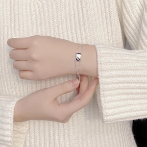 Detail of silver quilted rectangle bracelet with double chain on white sweater