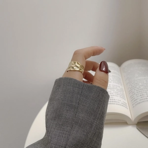 Detail of a wide gold-tone ring with irregular hammered texture on female finger