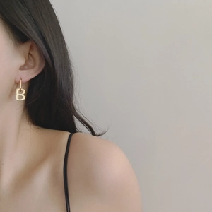 Close-up of a gold letter B pendant earring worn on a model for a vintage look