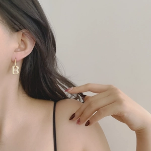 Close-up of a minimalist golden letter B drop earring on model with sleek metallic finish