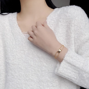 Close-up of a gold-toned quilted pattern rectangular bracelet on a soft knit sleeve