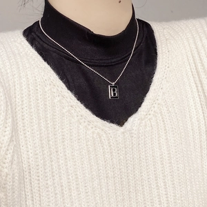 Detail shot of a square silver-edged pendant with black enamel B letter on bead chain