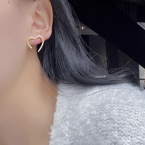 Close-up of minimalist gold hollow heart earrings worn by a model in soft lighting