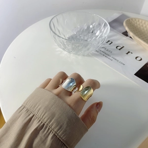 Close-up of wavy irregular wide rings in gold and silver finish on a hand