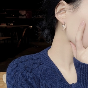 Detail of silver S-curve spiral earrings worn by a model in a navy blue sweater