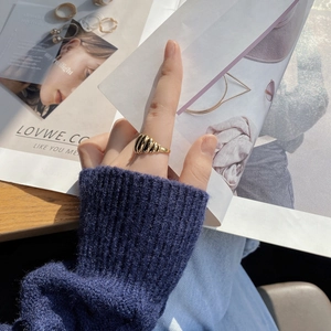 Detail of a golden croissant ring with spiral texture worn on index finger over blue knitwear
