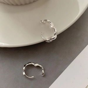 Dettaglio di orecchini a cerchio intrecciati in argento con trama elegante su piatto