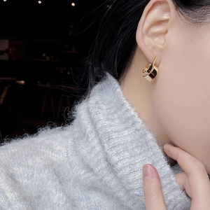 Macro view of gold S-curve twisted earrings paired with a cozy autumn knit sweater