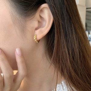 Primo piano di orecchini a cerchio intrecciati dorati indossati da una modella elegante
