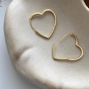 Détail de boucles d'oreilles cœur dorées montrant le fermoir sur une plaque céramique