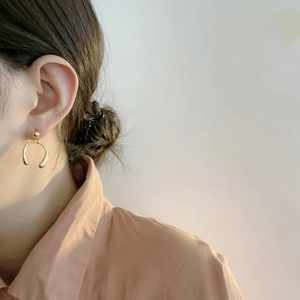 Détail de boucles d'oreilles fer à cheval dorées portées par un mannequin au style épuré