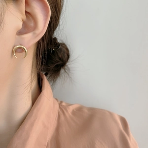 Close-up of a polished gold crescent moon earring worn by a model in a minimalist style