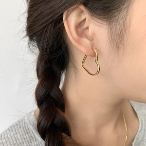 Gros plan d'élégantes boucles d'oreilles créoles dorées en forme de cœur portées par un modèle