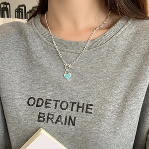 Detail of sky blue enamel heart pendant on silver toggle clasp chain worn by model