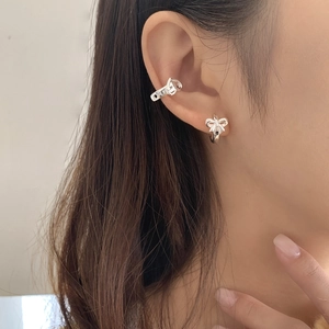 Macro shot of silver bow stud and textured ear cuff set on model ear