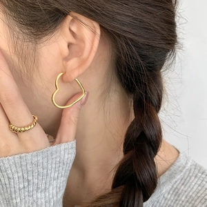 Détail de boucles d'oreilles cœur dorées et bague torsadée sur mannequin en tricot