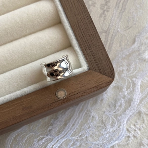 Macro view of silver wide ring with irregular liquid metal texture on white velvet
