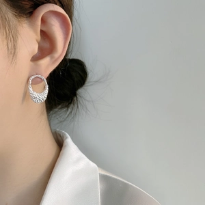 Detailed close-up of textured sterling silver oval earring with hammered surface on ear
