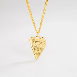 Close-up of golden irregular heart pendant featuring a minimalist smile and textured surface