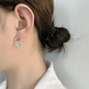 Macro detail of silver geometric oval earrings with lava texture on woman model