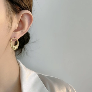Close-up of gold lava texture oval earrings worn by a model in a minimalist style