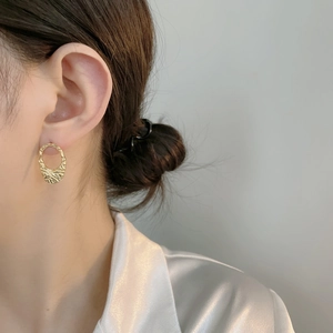 Close-up of golden irregular oval earrings with hammered texture on female model