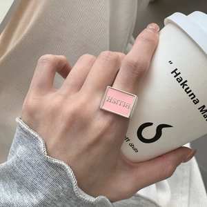 Close-up of a silver ring with pink enamel detail and BLUSH engraving on a finger