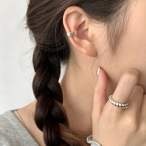 Close-up of a minimalist three-layer silver ear cuff and textured twisted silver ring