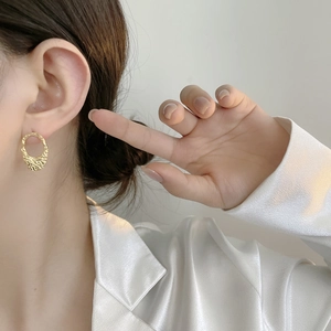 Close-up of gold geometric earrings with lava texture on woman's earlobes