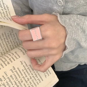 Detail of pink enamel BLUSH ring on hand with aesthetic book background and soft lighting