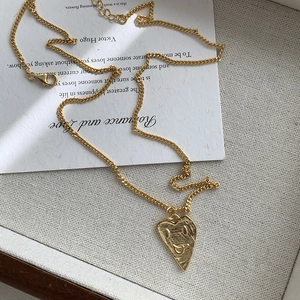 Detail of gold heart pendant with textured smiling face and thin link chain on cloth